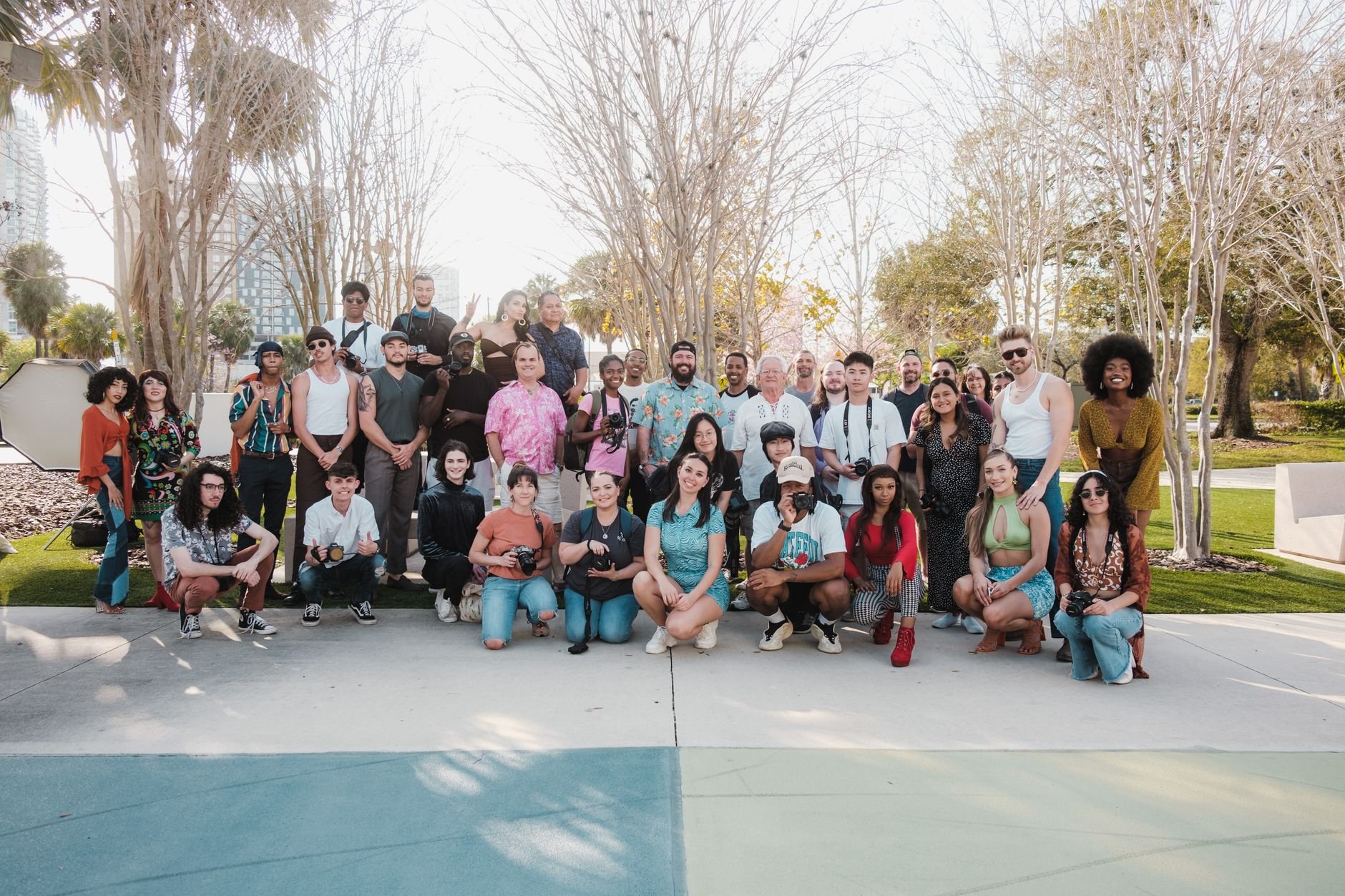 A diverse group of adults posing together outdoors in a park on a sunny day.